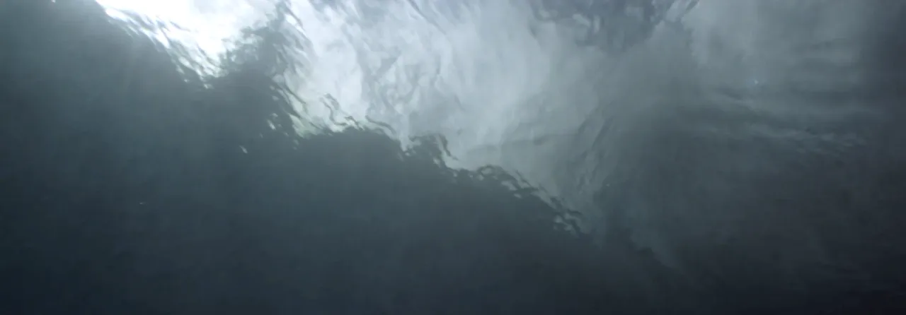 Blick von unten auf die Wasseroberfläche eines Sees, das Licht bricht sich in den Wellen